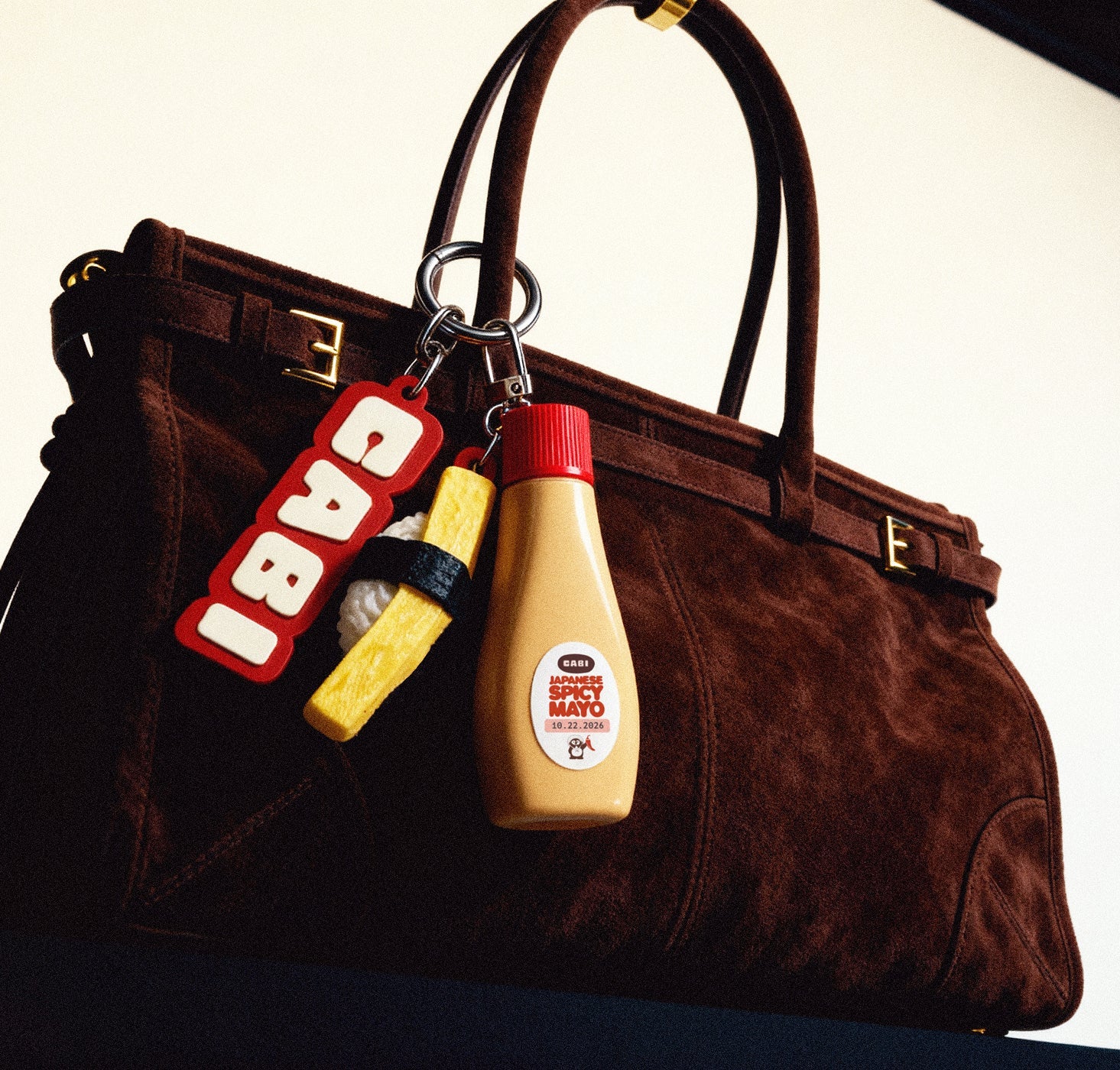 Brown handbag with mustard and mayonnaise bottle keychains on a white background