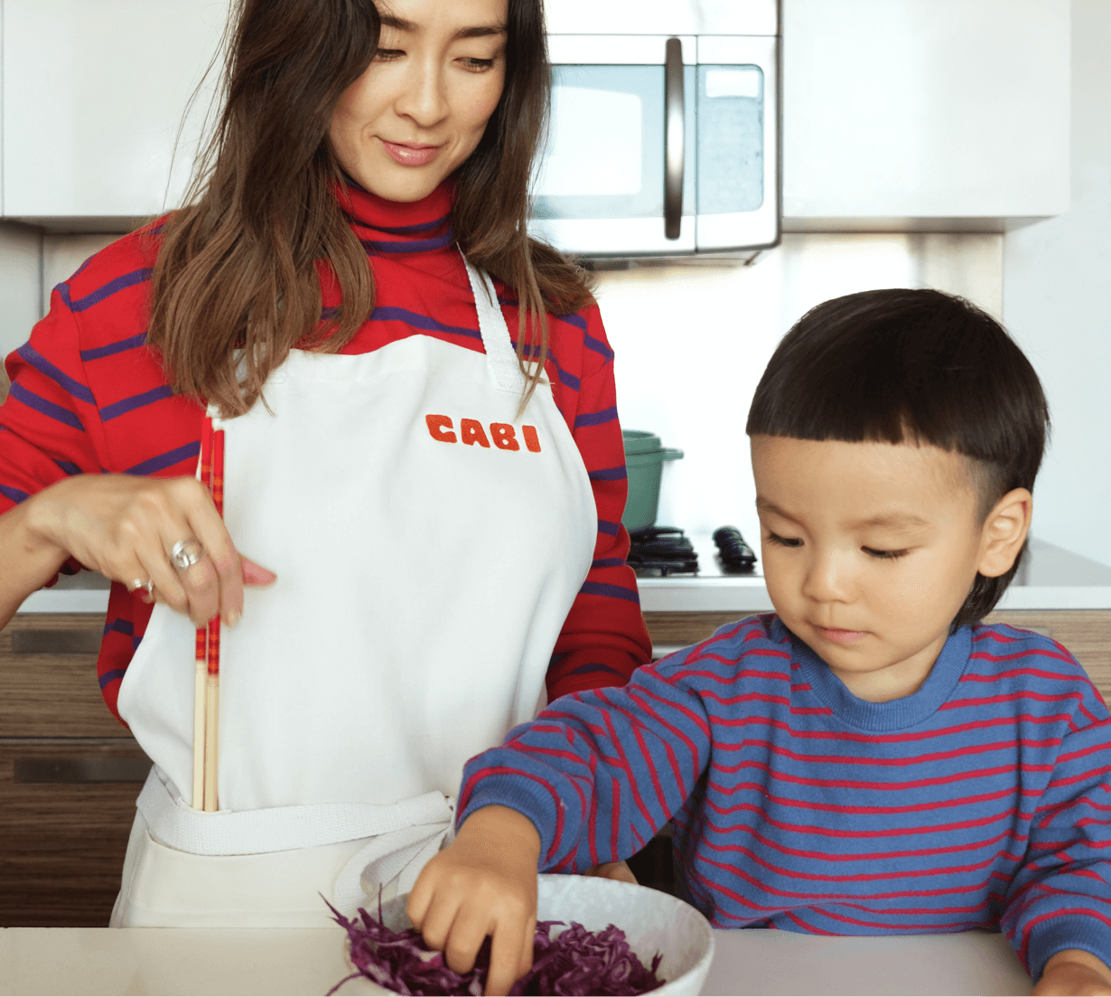 A woman wearing a Cabi apron with a kid touching food