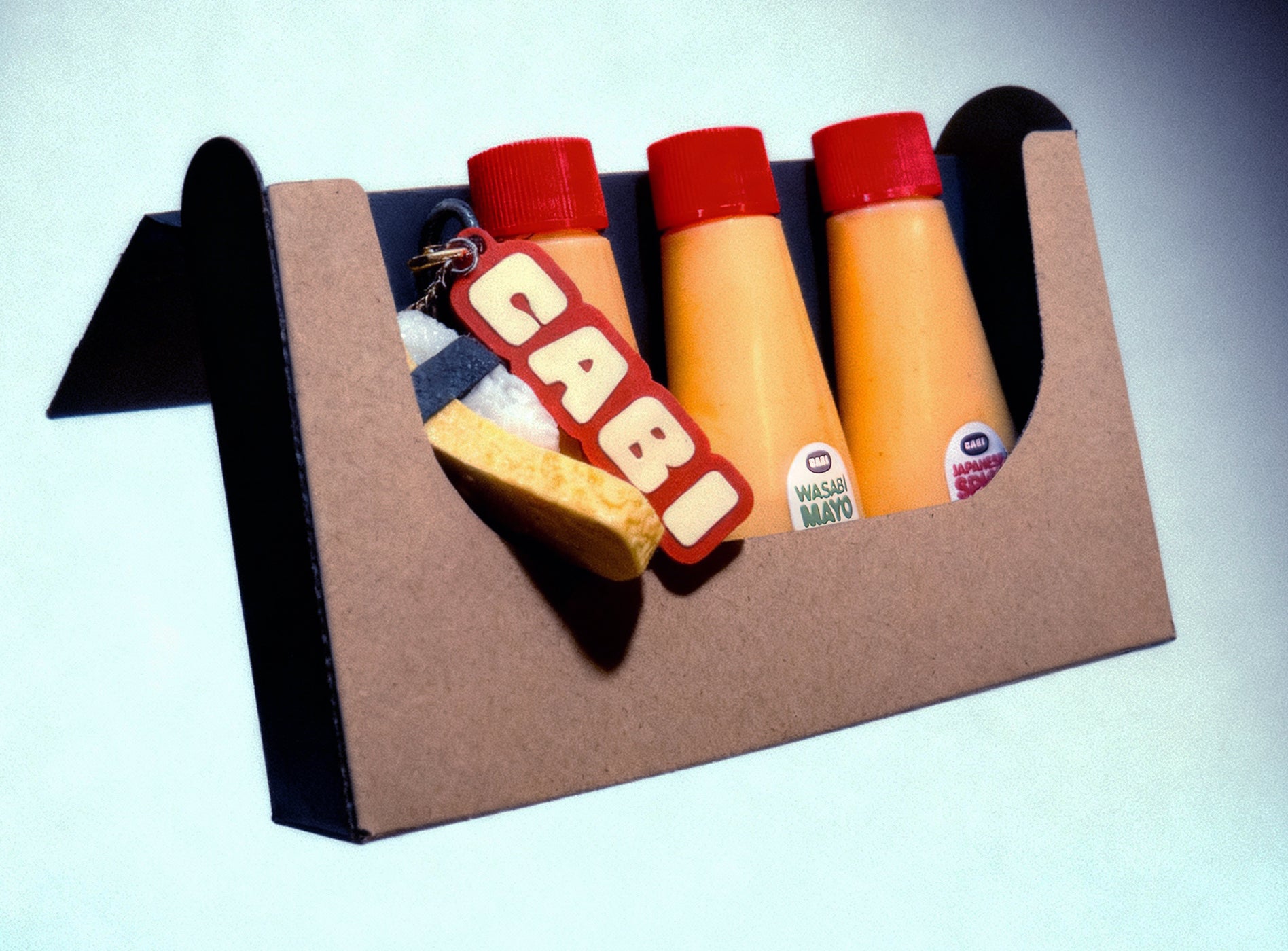 Cabi mayonnaise bottles in a cardboard holder on a light blue background