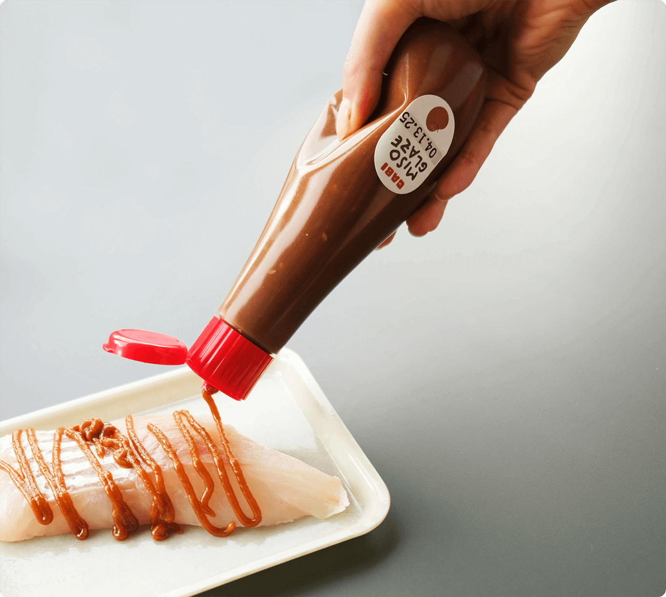 Cabi Miso Glaze drizzled over raw fish fillet on a white plate.